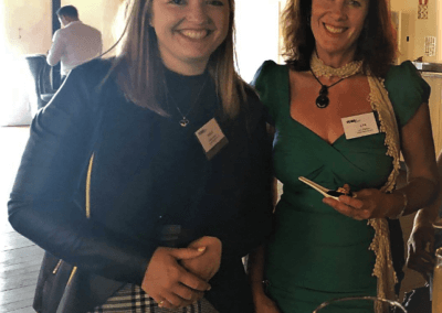 Two women stand together smiling with a chandelier style light in the background