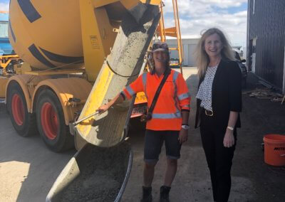 Two people stand in front of a concrete mixer smiling